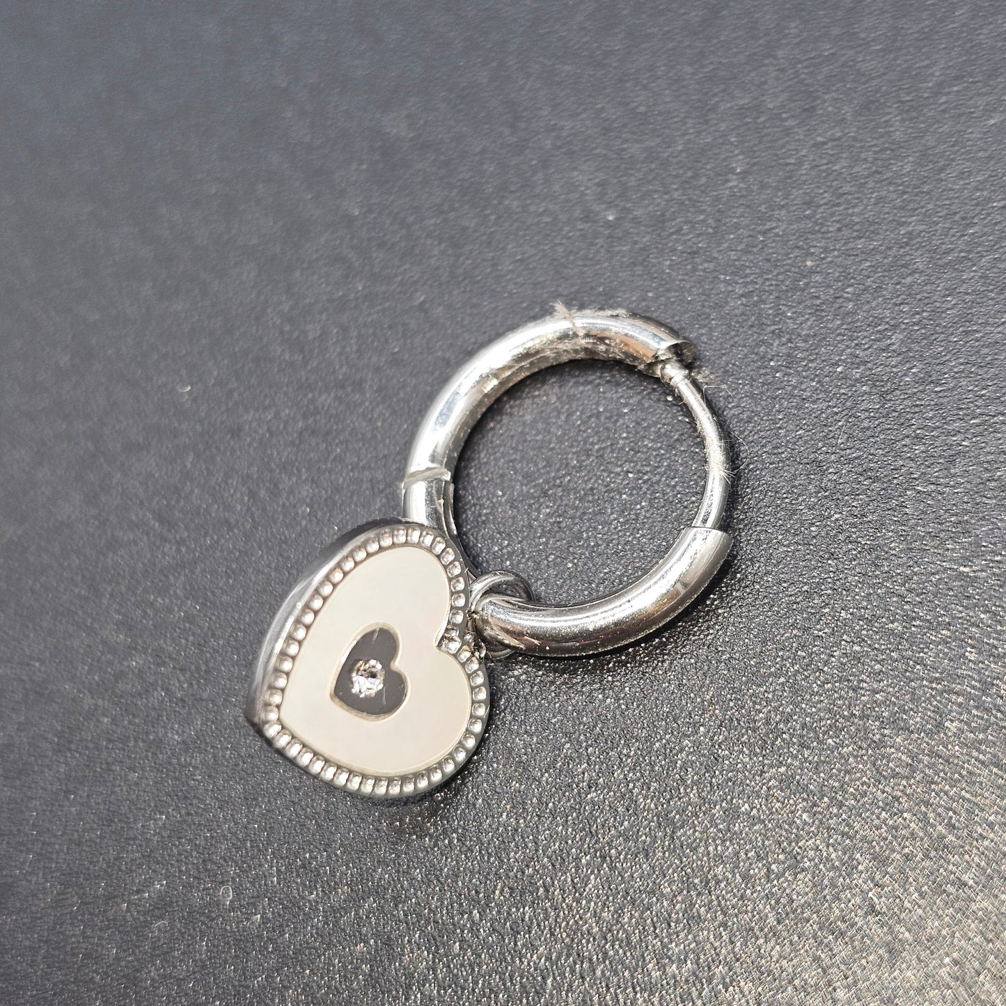 Boucle d’oreille argentée en forme de cœur avec contour perlé et centre ajouré.