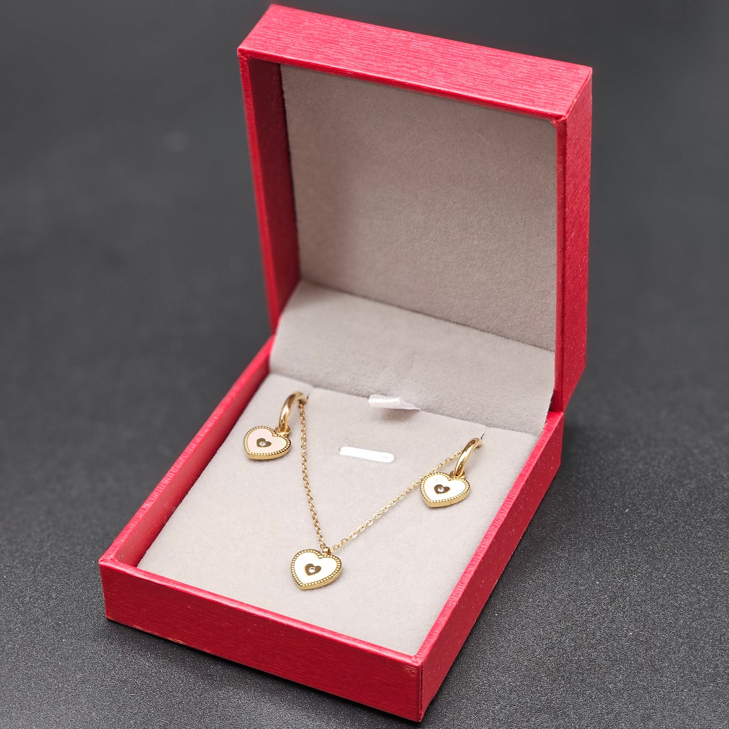 Détail du collier et des boucles dorées en forme de cœur dans la boîte rouge.