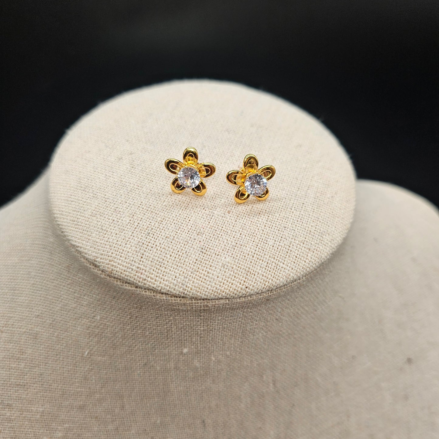 Vue rapprochée des boucles d’oreilles fleurs dorées, détail de la monture et éclat du cristal.