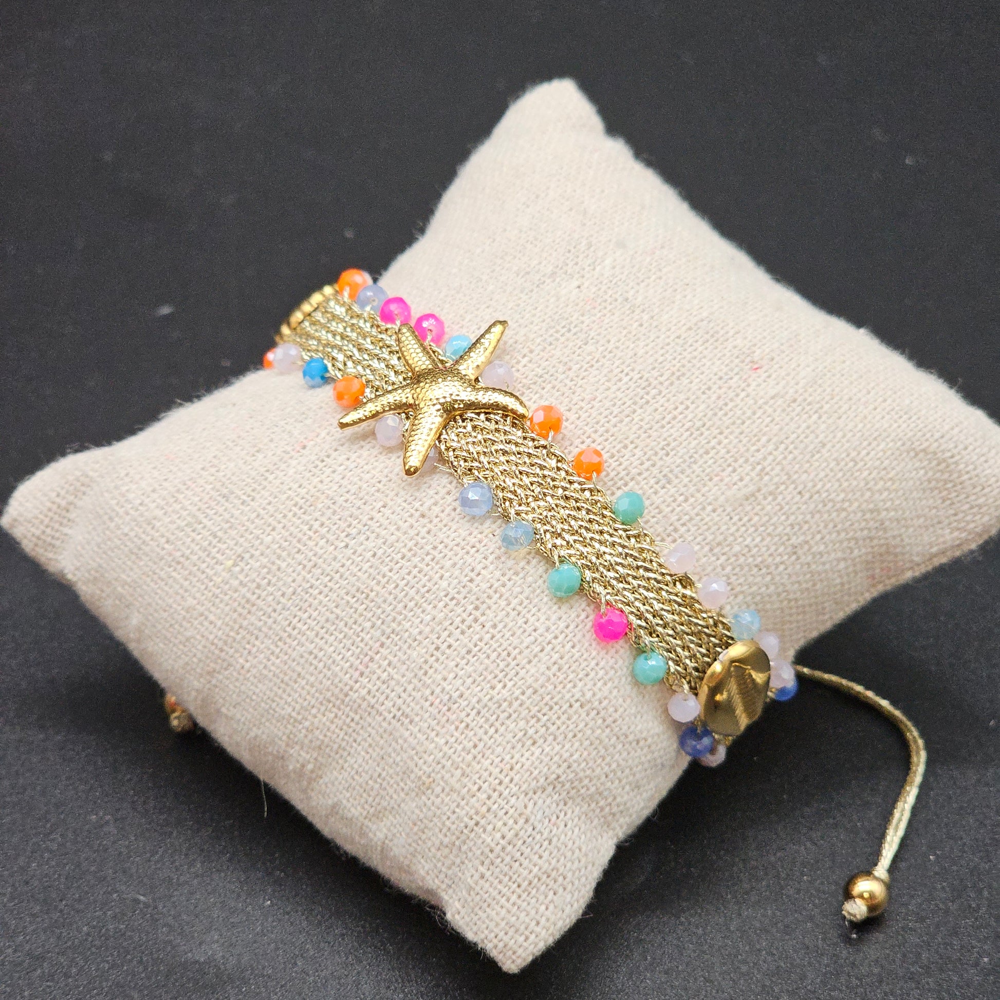 Bracelet doré orné d’une étoile de mer et de perles multicolores sur coussin de présentation – Bijoux Nice.