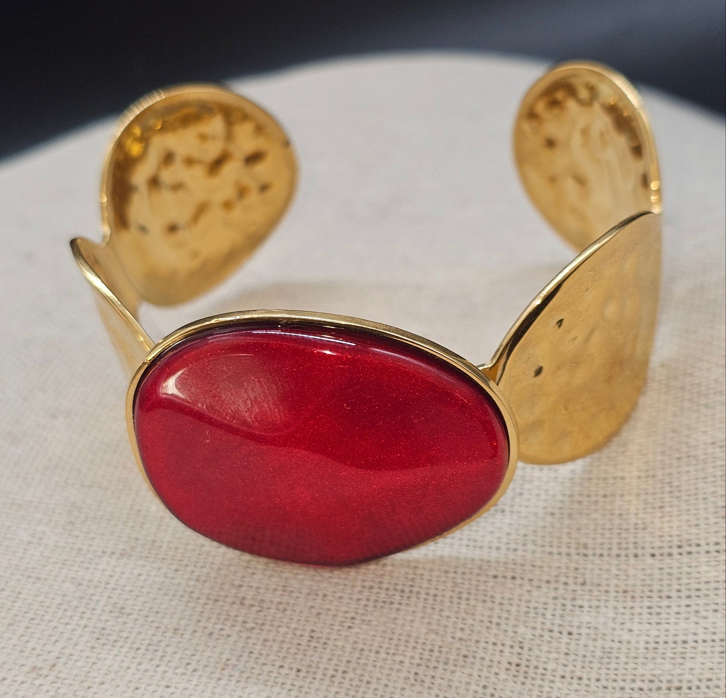 Bracelet manchette dorée orné d’une pierre rouge éclatante sur fond clair.