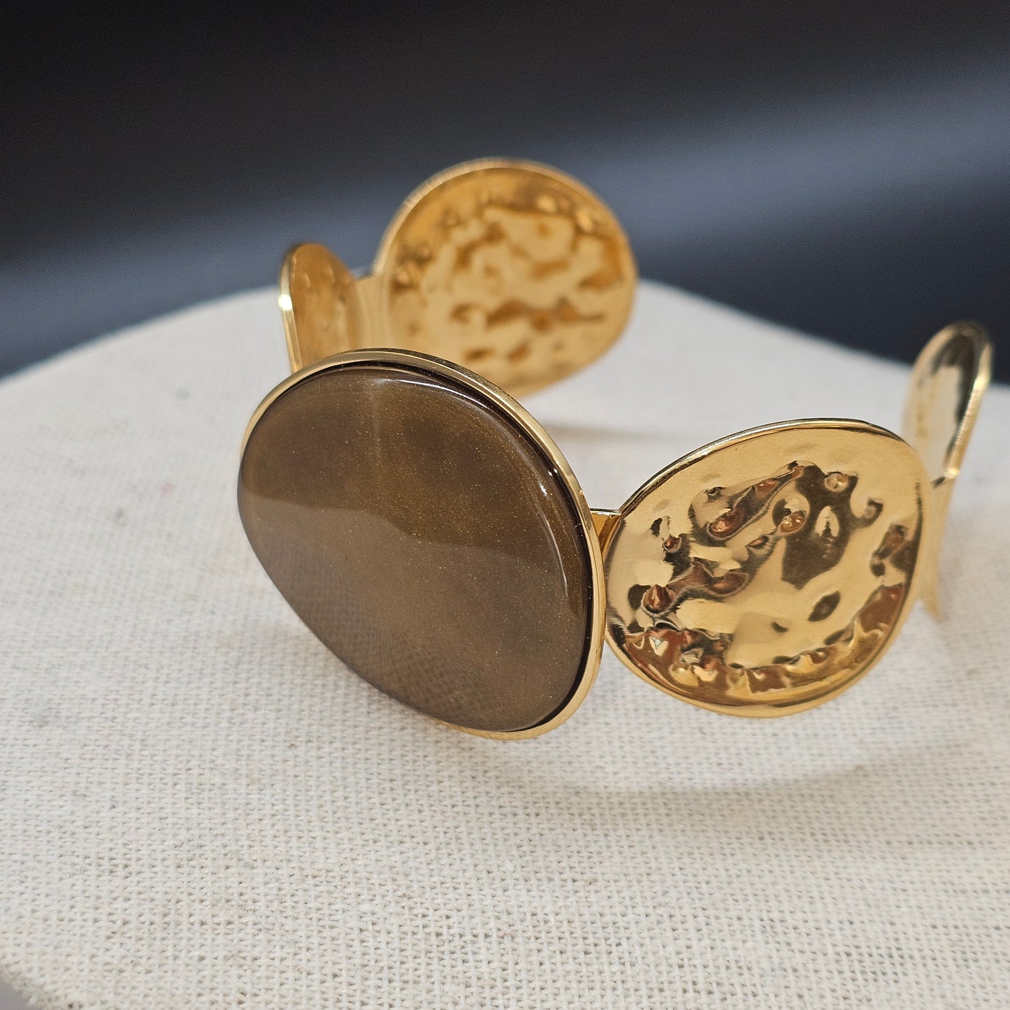 Bracelet manchette dorée avec pierre verte scintillante et finition martelée.