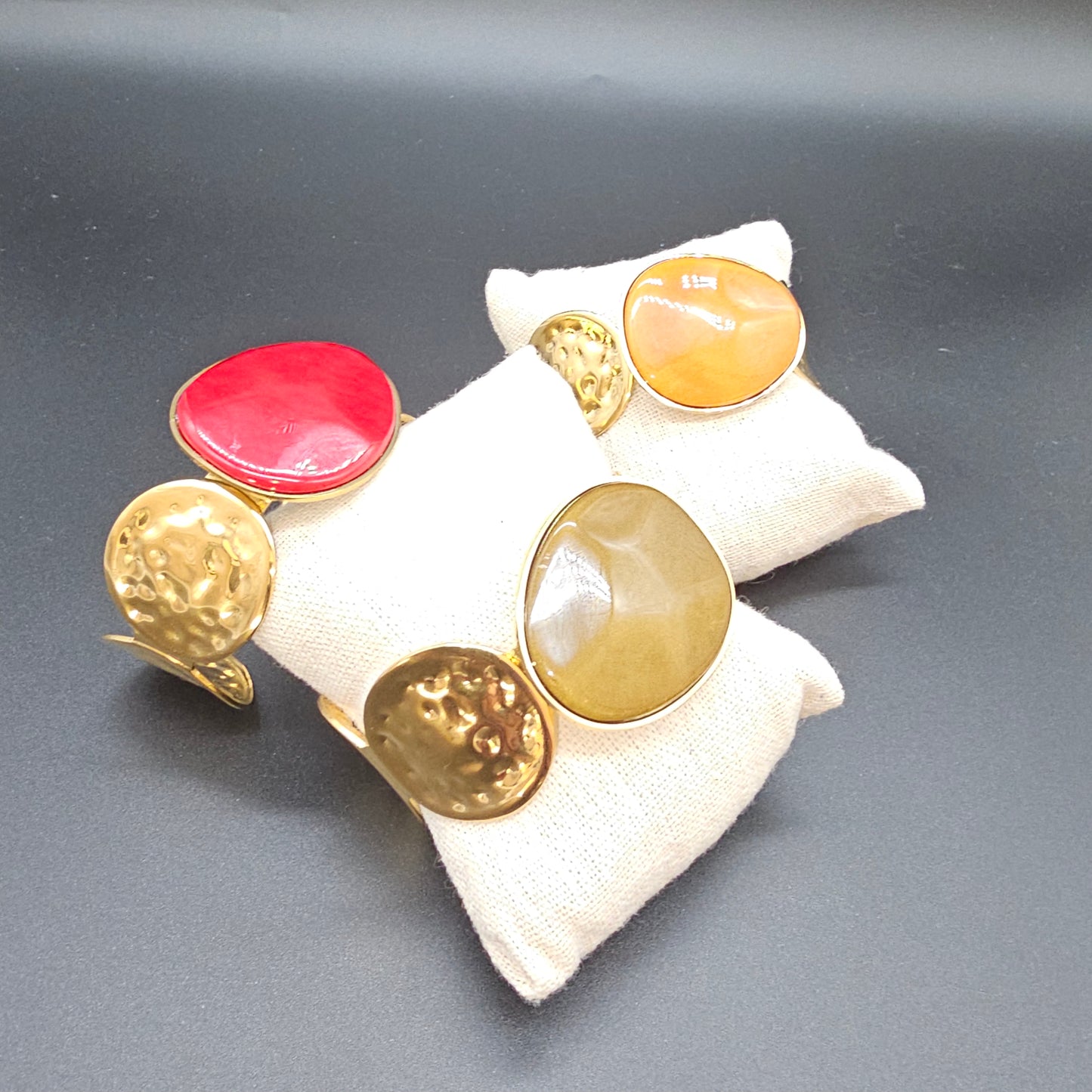 Trio de bracelets manchettes dorées avec pierres ocre, rouge et verte.