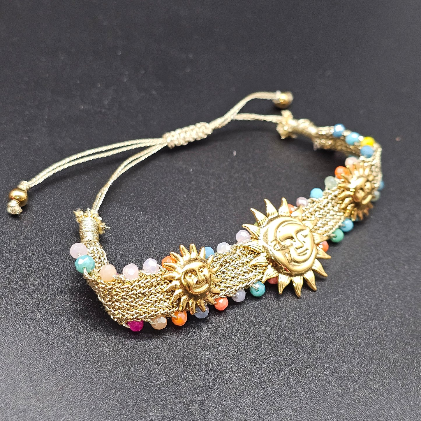 Bracelet doré motif soleil avec perles fines multicolores sur fond noir