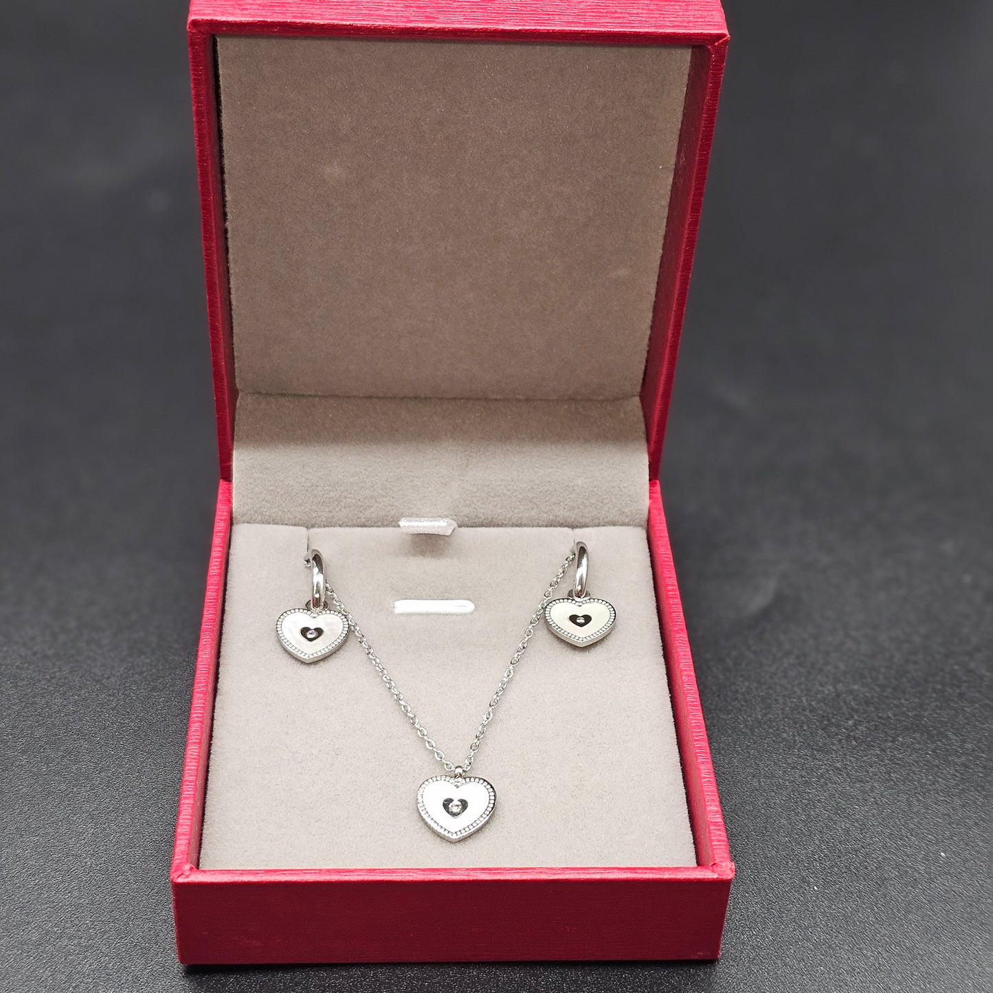 Coffret argenté complet avec collier et boucles d’oreilles cœur, présenté dans une boîte rouge élégante.