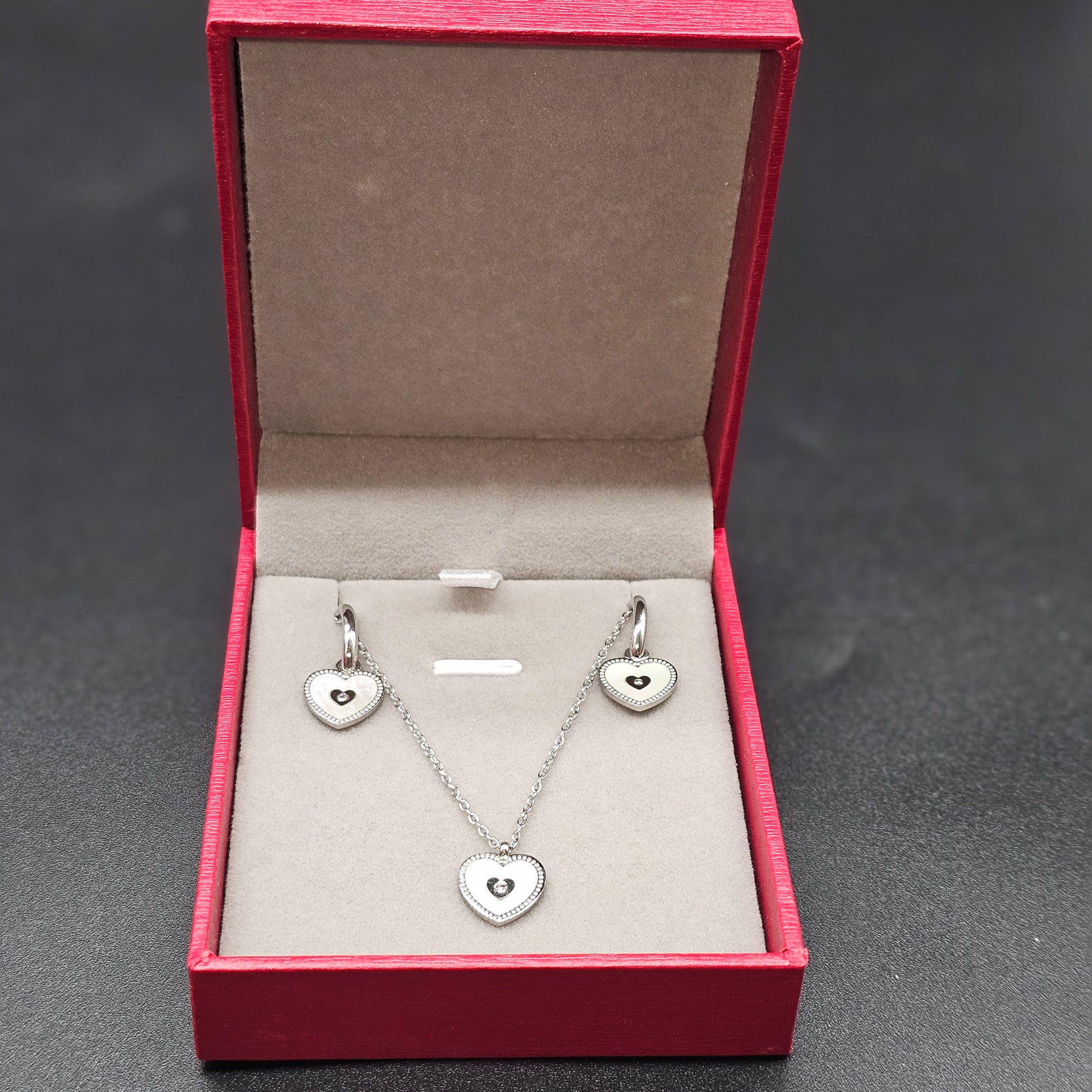 Coffret argenté complet avec collier et boucles d’oreilles cœur, présenté dans une boîte rouge élégante.