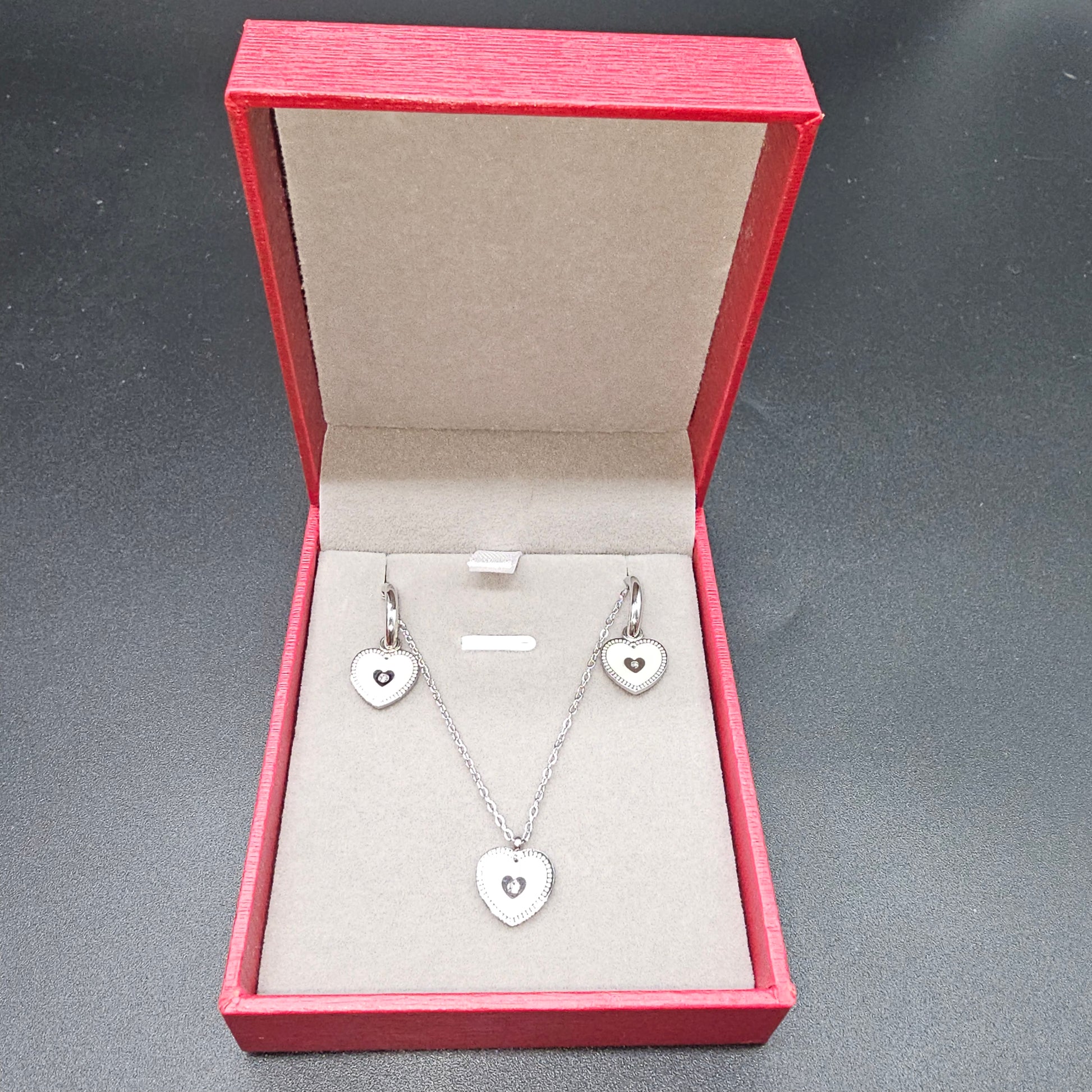 Coffret cœur argenté avec collier et boucles d’oreilles en acier inoxydable dans une boîte rouge ouverte.