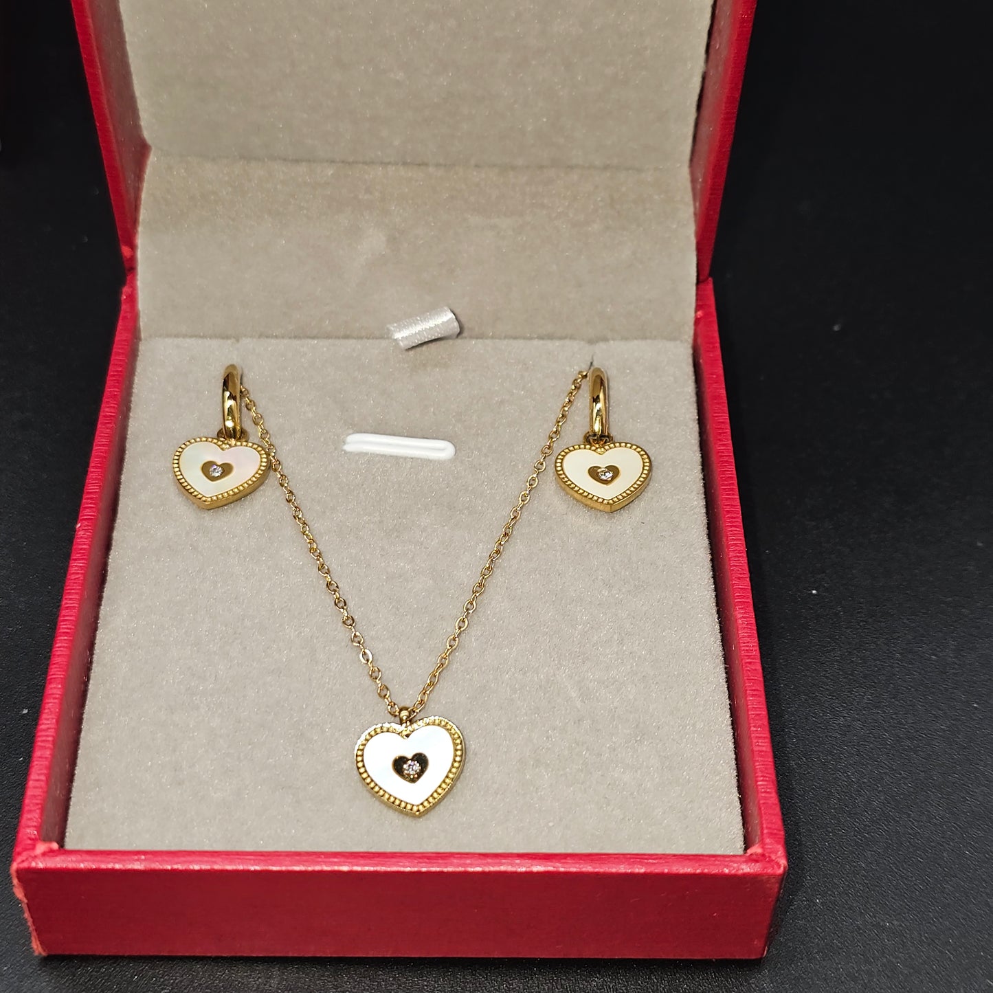 Coffret doré avec collier et boucles d’oreilles en forme de cœur dans une boîte rouge ouverte.