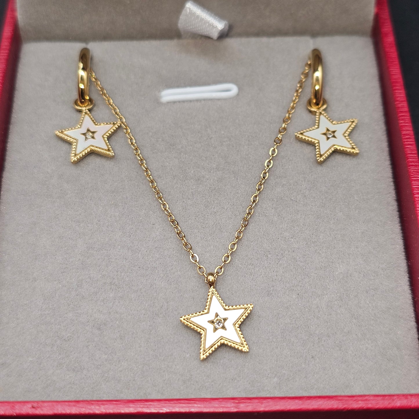 Collier Étoile Doré et boucles assorties sur fond rouge.