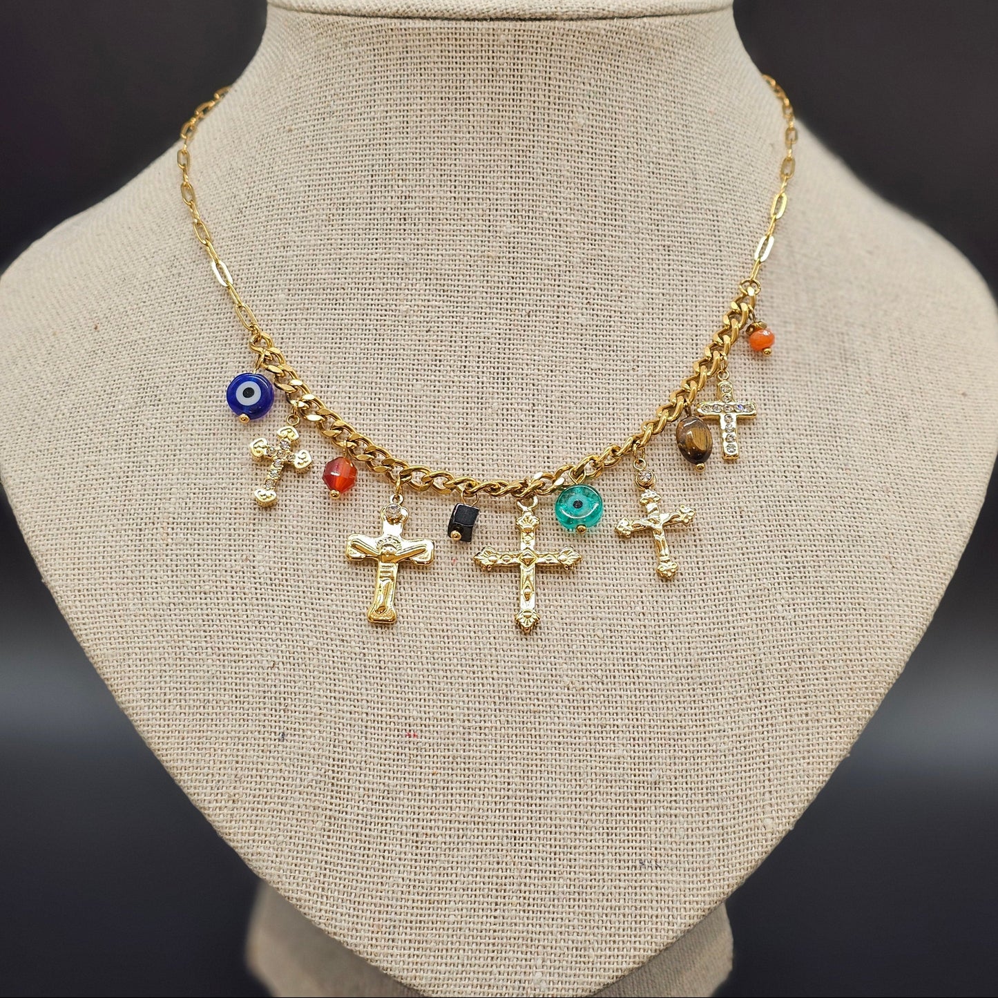 Collier doré orné de charms croix et perles colorées, présenté sur buste beige.