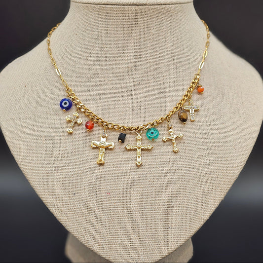 Collier doré orné de charms croix et perles colorées, présenté sur buste beige.
