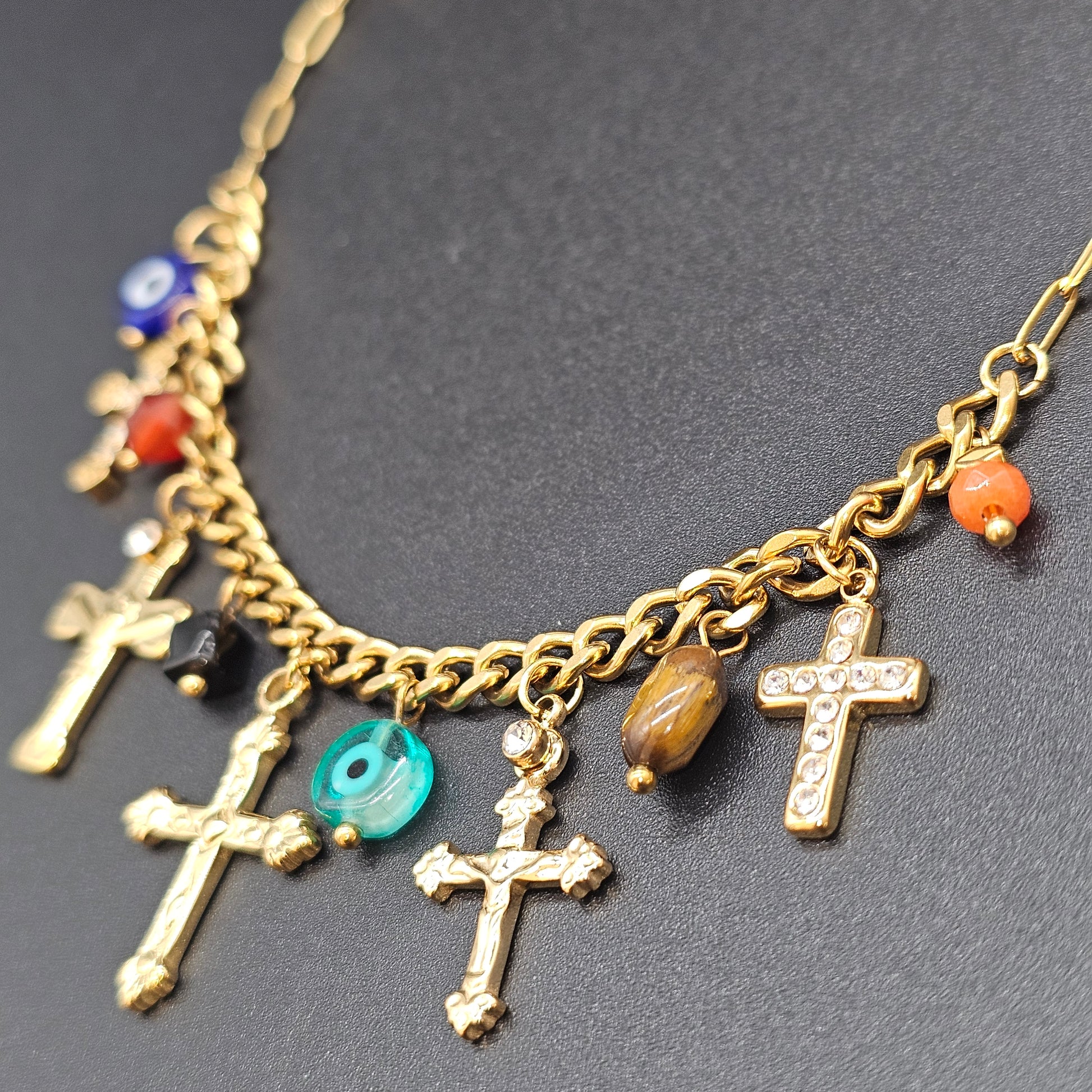 Zoom sur les pendentifs croix dorées et perles colorées du collier, sur fond noir mat.