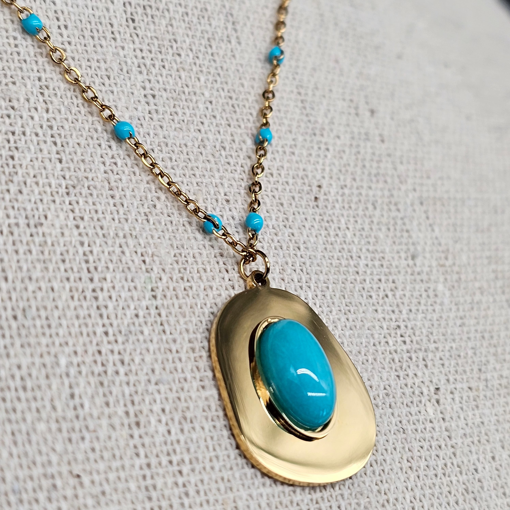 Détail du collier doré orné d’une pierre turquoise sur chaîne à perles bleues, style bohème chic.