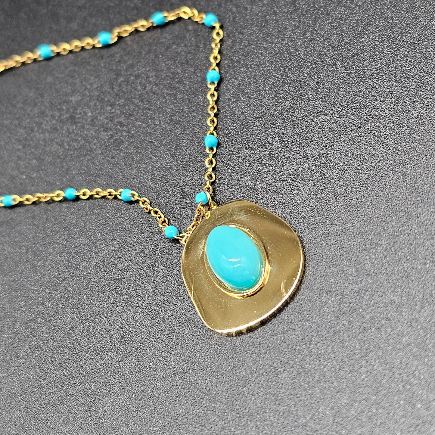 Gros plan sur le pendentif doré en forme irrégulière avec pierre turquoise centrale.