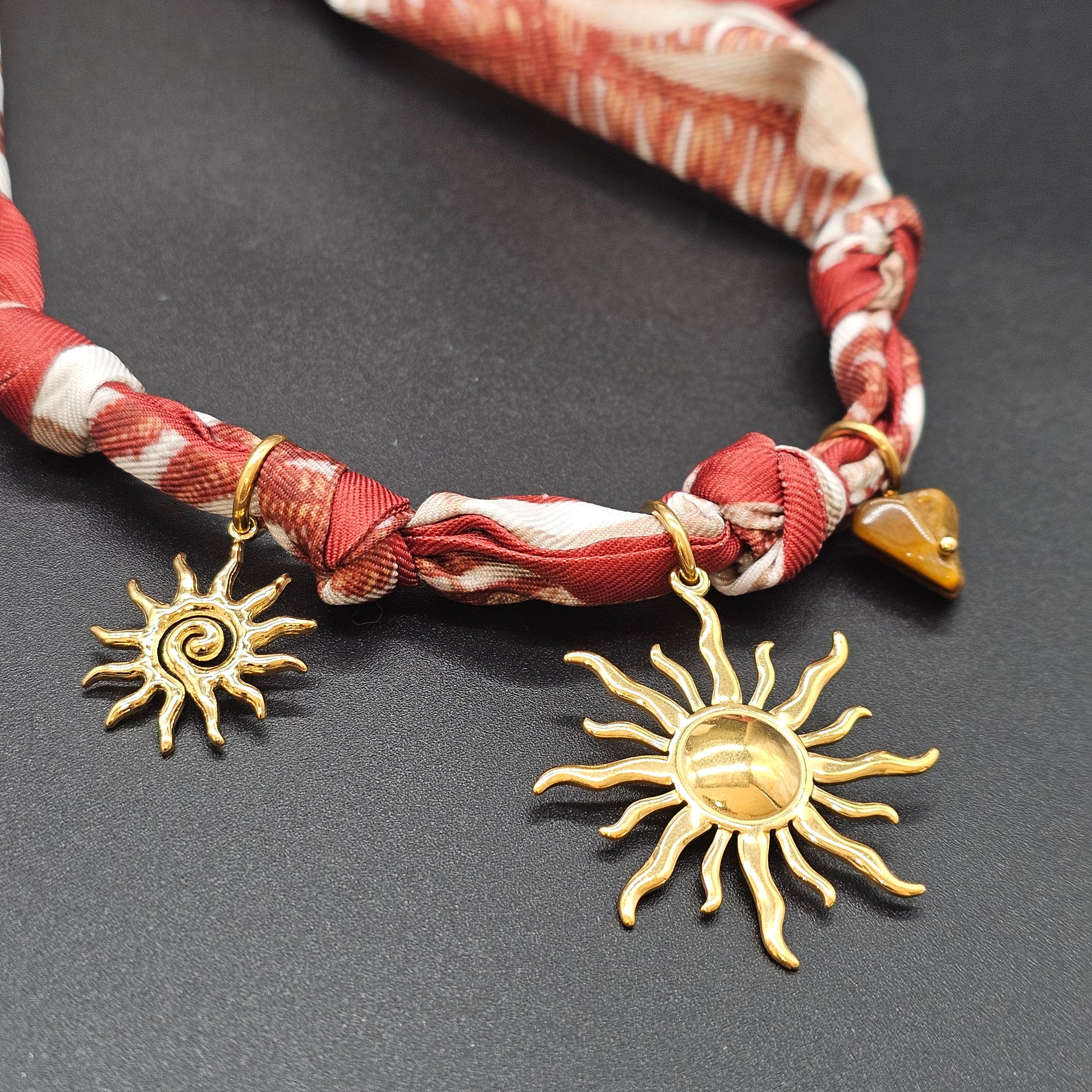 Gros plan macro sur pendentifs dorés et nœud du foulard.