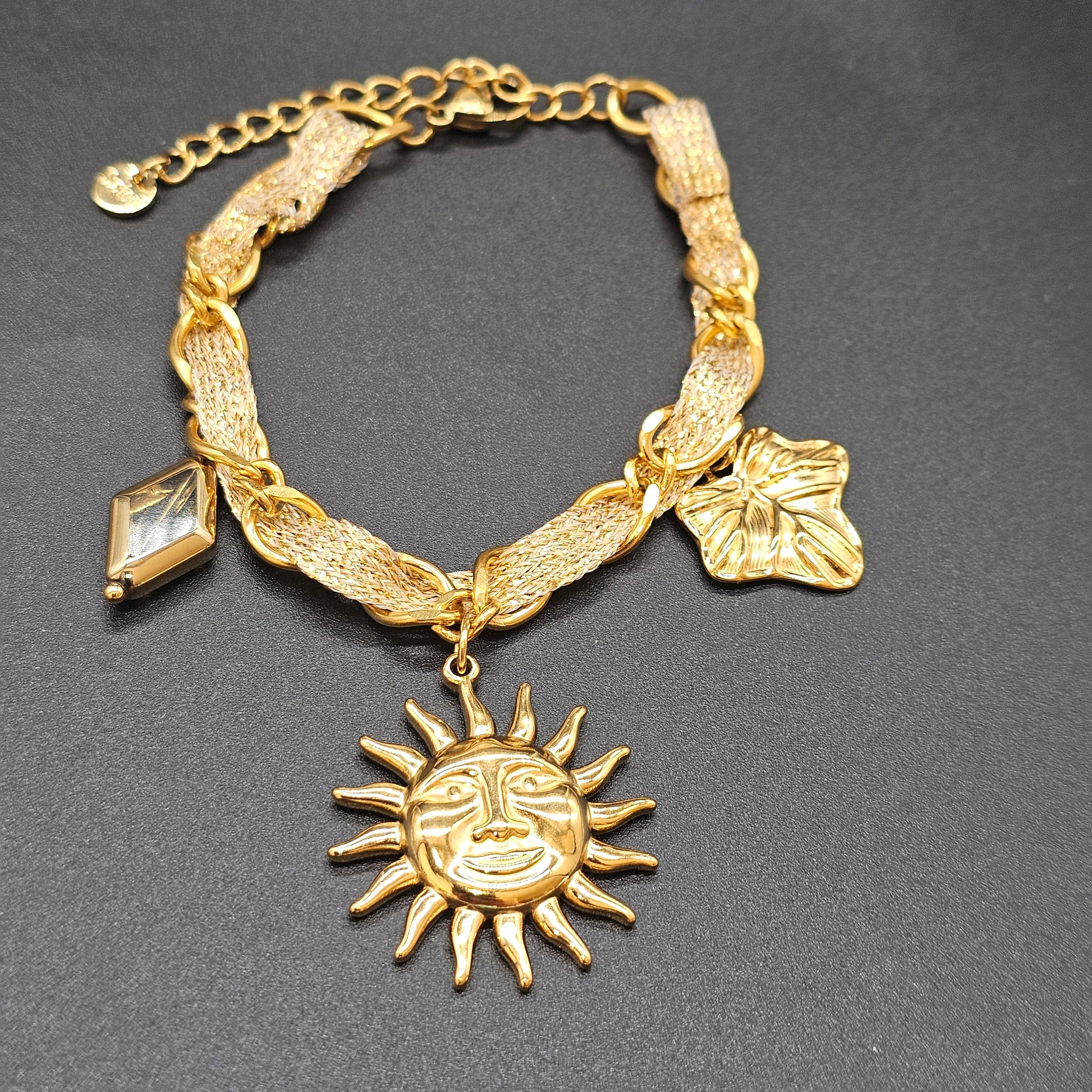 Gros plan sur le bracelet doré avec pendentif soleil et pampilles.